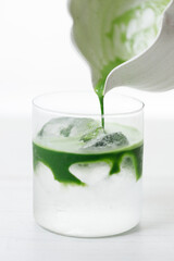 fresh matcha tea, green tea pouring on a glass of coconut water on white wooden table.