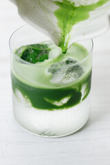 fresh matcha tea, green tea pouring on a glass of coconut water on white wooden table.