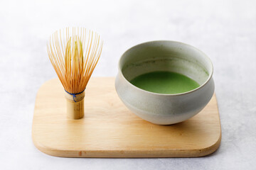 Cup of fresh matcha tea, green tea and Chasen, bamboo whisk, on wooden plate on white table.