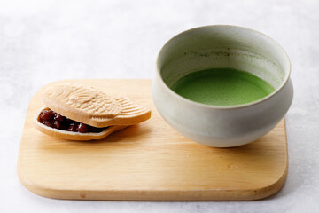 Cup of fresh matcha tea, green tea and Taiyaki, Japanese fish-shaped cake, filled with Anko or red bean on wooden plate.