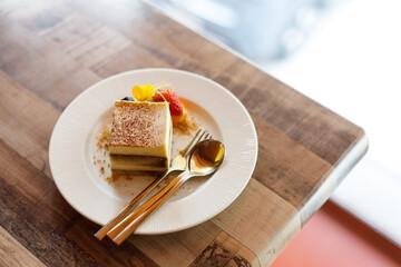 Freshly tiramisu cake on white ceramic plate decorated with fruit and edible flowers on wooden table background.