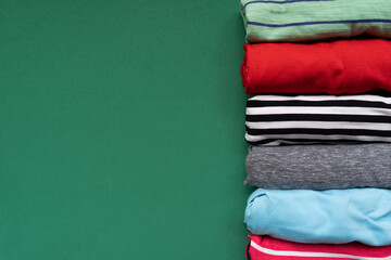 close up of rolled colorful t shirt clothes on green table background, travel and lifestyle concept