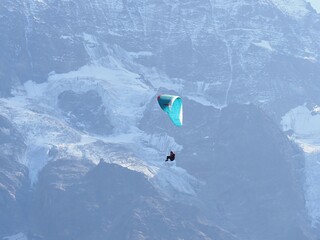 Paraglider flying over snow-covered alpine mountain range