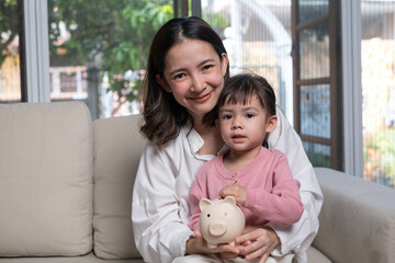 A mother and daughter smile together while holding a piggy bank, symbolizing saving and financial...