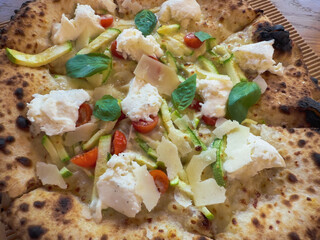A hot pizza is topped with mozzarella, cherry tomatoes, zucchini, and fresh basil, showcasing a perfect blend of flavors.