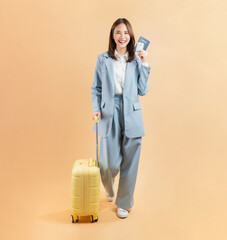 Happy Asian business woman holding passport and credit card with suitcase isolated on beige color background.