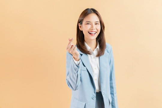 Cheerful beautiful Asian business woman showing mini heart sign on beige color background, love concept. - Powered by Adobe