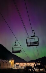 Ski lift chairs silhouetted against a vibrant aurora borealis in the night sky