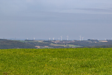 Sustainable energy: Wind turbines on the horizon above green meadows and forests