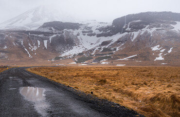 Wet asphalt road leading to snowy mountains in iceland