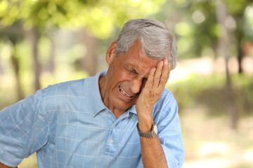 Senior tired man covering one eye with hands feeling more painful while standing on park. crying Itchy eyes from allergy. Concept Cataract Surgery.