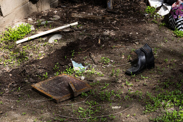 Worn black boot on dirt ground surrounded by trash, plants, and debris
