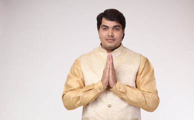 Portrait of a Young Indian man holding hands with namaste gesture - greeting guests on white with...