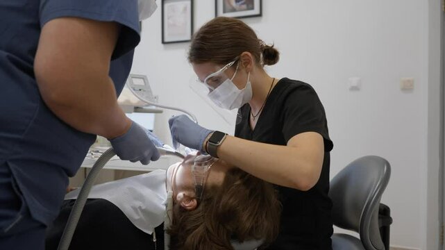 A dentist and assistant work in tandem using four-handed dentistry. The doctor drills with a mirror while the assistant manages water irrigation and suction for a precise, clean procedure.