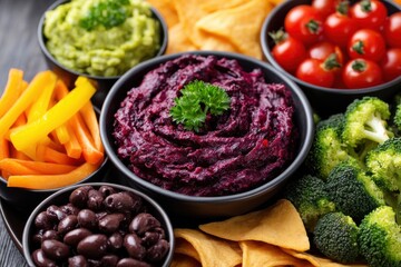 Colorful gourmet vegetable platter featuring vibrant dips with beetroot hummus, creamy guacamole, fresh broccoli, assorted carrots, and crispy tortilla chips arranged on a dark wooden background
