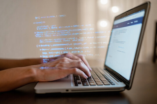 Close up of hands typing code on a laptop at night with glowing code overlay