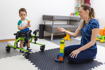 Physical therapist assists a young boy with movement disorders as he engages in physical...