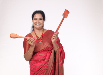 Fototapeta premium Indian happy woman holding wooden spatula. She wearing traditional saree showing kitchen items and home appliances products for cooking food. while standing isolated over white background
