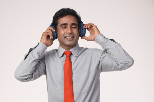 Indian happy young corporate business man listening to music through headphones