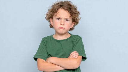Young boy is wearing a green shirt and has his arms crossed. He looks unhappy and is frowning