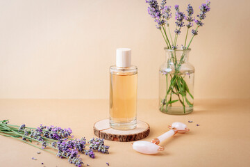 Glass cosmetic bottle with liquid and fresh lavender flowers on beige background. Closeup