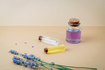 Hydrolat and essential oil bottles with lavender flowers on beige background. Closeup, copy space