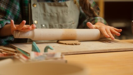 Talented creative teenage Caucasian little girl artist sculptor child ceramist kid student use wooden rolling pin rolls clay material preparing craft artwork sculpture ceramic pottery indoor workshop