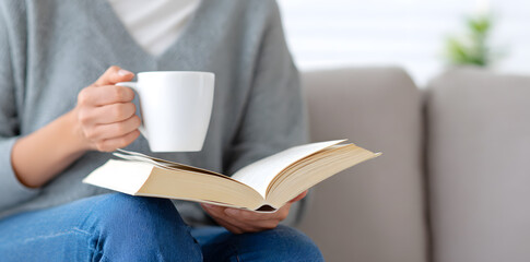 Close-up woman relaxing with a cup of tea and reading a book at home. Peaceful and cozy scene of enjoying quiet time.