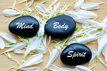 Three stacked stones with mind and body text beside white petals
