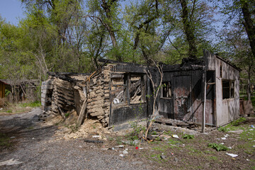 Burned and partially collapsed house in forested area, with charred walls and debris around