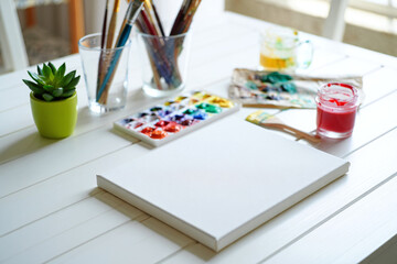 Artistic workspace with blank canvas watercolor paints brushes and a small potted plant
