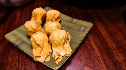 close up of six pieces of uncooked raw shrimp and pork stuffed dumplings on a plate on a wooden table with copy space