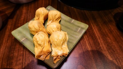 close up of six pieces of uncooked raw shrimp and pork stuffed dumplings on a plate on a wooden table with copy space