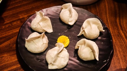 close up of six uncooked raw pork dumplings (Jiaozi or Gyoza) on a plate with a yellow flower in the middle for decoration