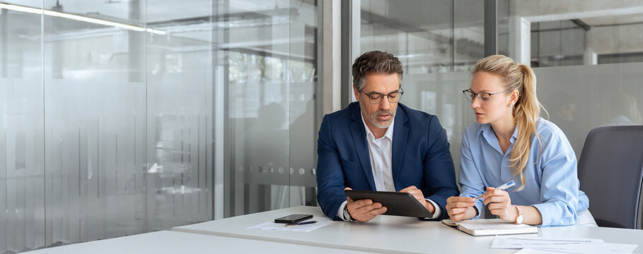Two professional business people working together. Partners mature man and woman discussing project in office. Team leader explain trainee working process using tablet pc computer. Banner, copy space - Powered by Adobe