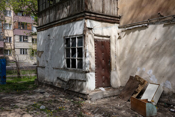 Old damaged building corner with broken window, worn-out door, and scattered debris outside
