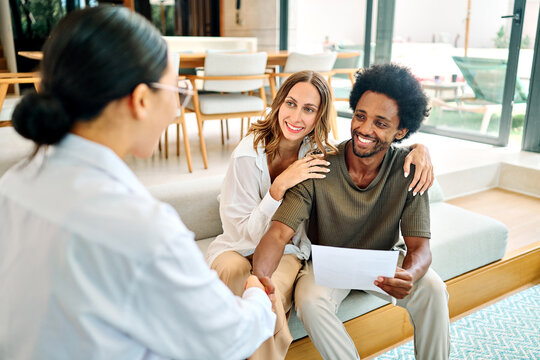 Young happy couple and an agent in a new property shaking hands or with advisor in office