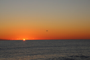 horizon in Black sea and a flying landing plane in the yellow orange sky against the background of...