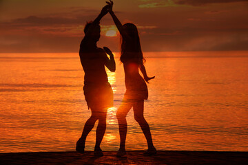 latin hispanic couple is dancing bachata above sea on summer sea beach Sunset over water. Two...