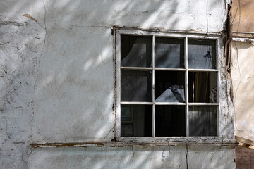 Broken window in old cracked wall with peeling paint and visible interior shadows