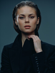 serious woman with wet hair wearing black jacket looks confidently at camera with neutral...