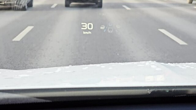 A car is driving down a road with a speedometer showing a speed of 29 mph. The car is surrounded by other cars on the road