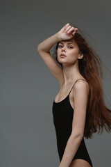 Young woman with long red hair in black bodysuit posing elegantly against gray background, showing...
