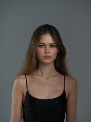 Fototapeta premium young woman with long brown hair wearing black tank top looking confidently at camera on gray background with soft lighting and natural expression