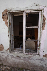 Close-up of broken window in abandoned building with peeling paint and visible debris inside.