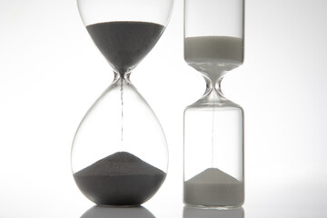 A sleek hourglass with dark sand flowing against a stark white background, symbolizing time. Ideal...