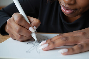 Close-up of a creative african american woman's hands drawing a character sketch with a white stylus, an artist or designer working on an illustration or cartoon concept