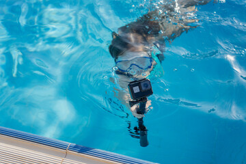 Girl swim underwater holding action camera in pool, summer vacation concept