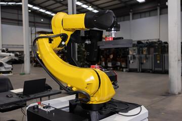 Yellow robotic arm lifting object in warehouse with laptop on table