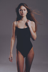 Young woman in black bodysuit posing confidently with flowing hair against gray background,...